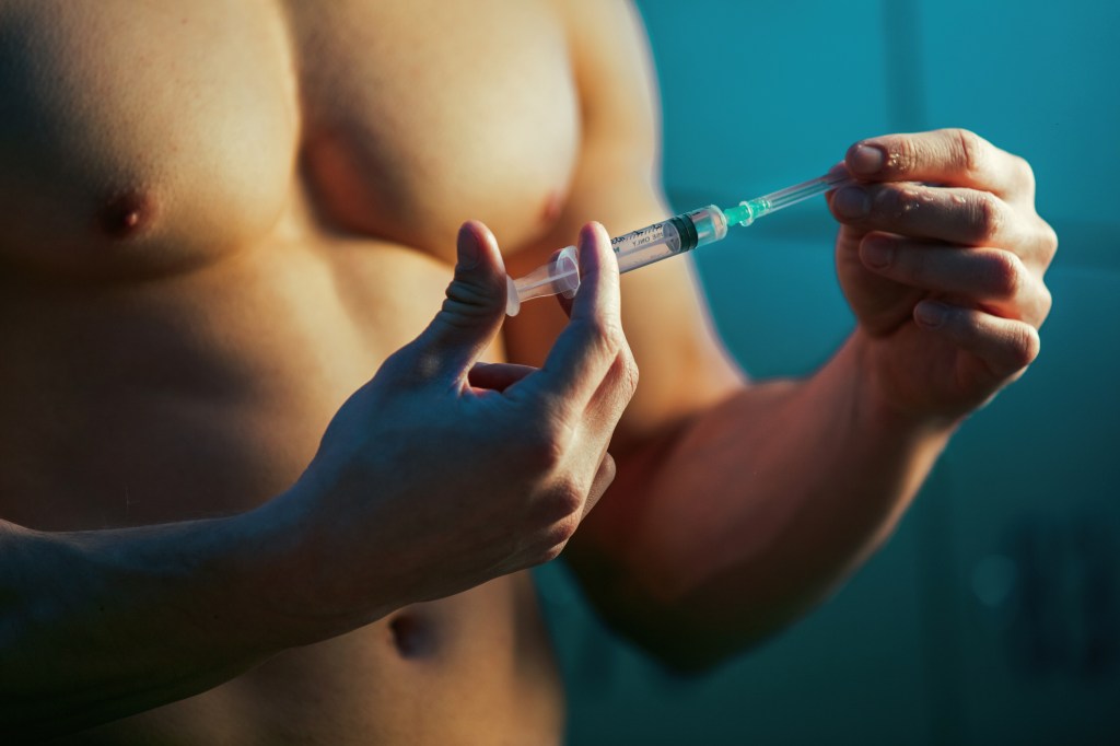 Close-up of a male bodybuilder preparing to inject performance-enhancing drugs in a locker room before training.